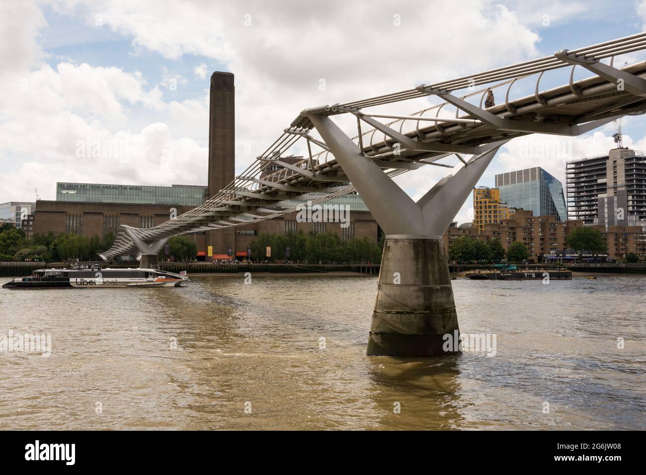Ein Uber-Boot, das unter der Millenium Bridge und der Tate Modern, London, England, Großbritannien, vorbeifährt. Stockfoto