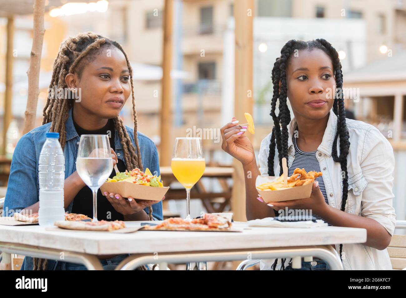 Neugierige afro-amerikanische Frauen halten Fast-Food-Tabletts auf einer Terrasse im Freien: Selektiver Fokus Stockfoto