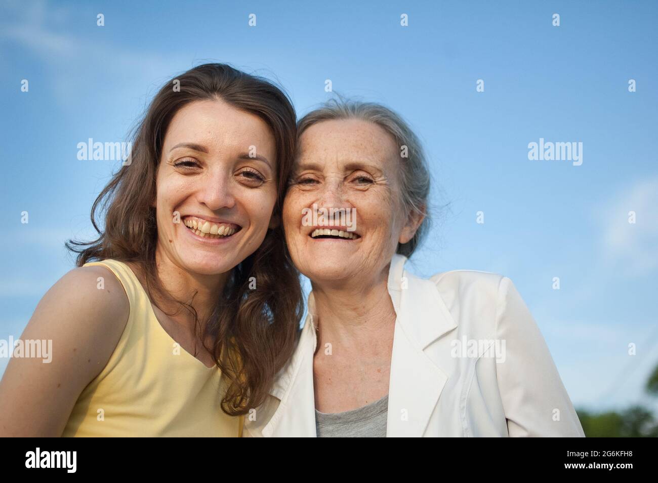 Ältere Mutter mit grauen Haaren und ihrer erwachsenen Tochter, die im Garten auf die Kamera schaut und sich an sonnigen Tagen im Freien umarmt, Muttertag Stockfoto