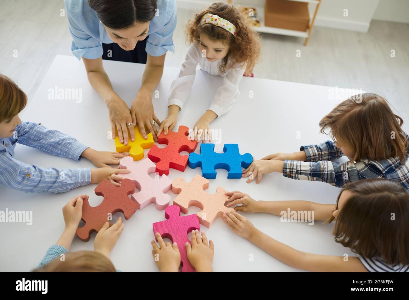 Team von kleinen Schulkindern mit Lehrer zusammen Puzzleteile Stockfoto