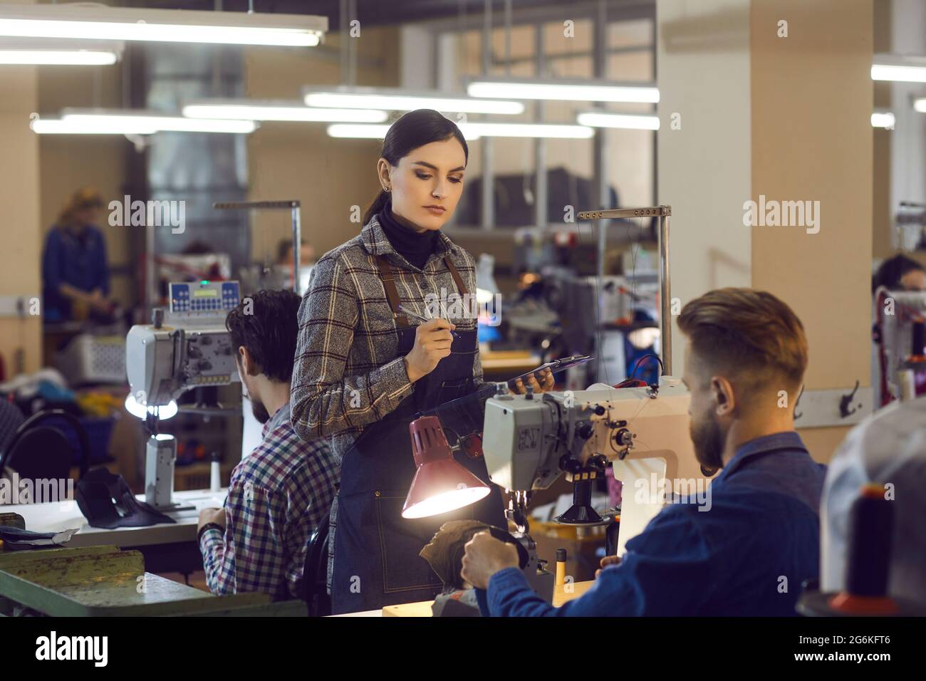 Weibliche Managerin, die die Qualität der Mitarbeiterarbeit in der Lederschuhfabrik überprüft Stockfoto