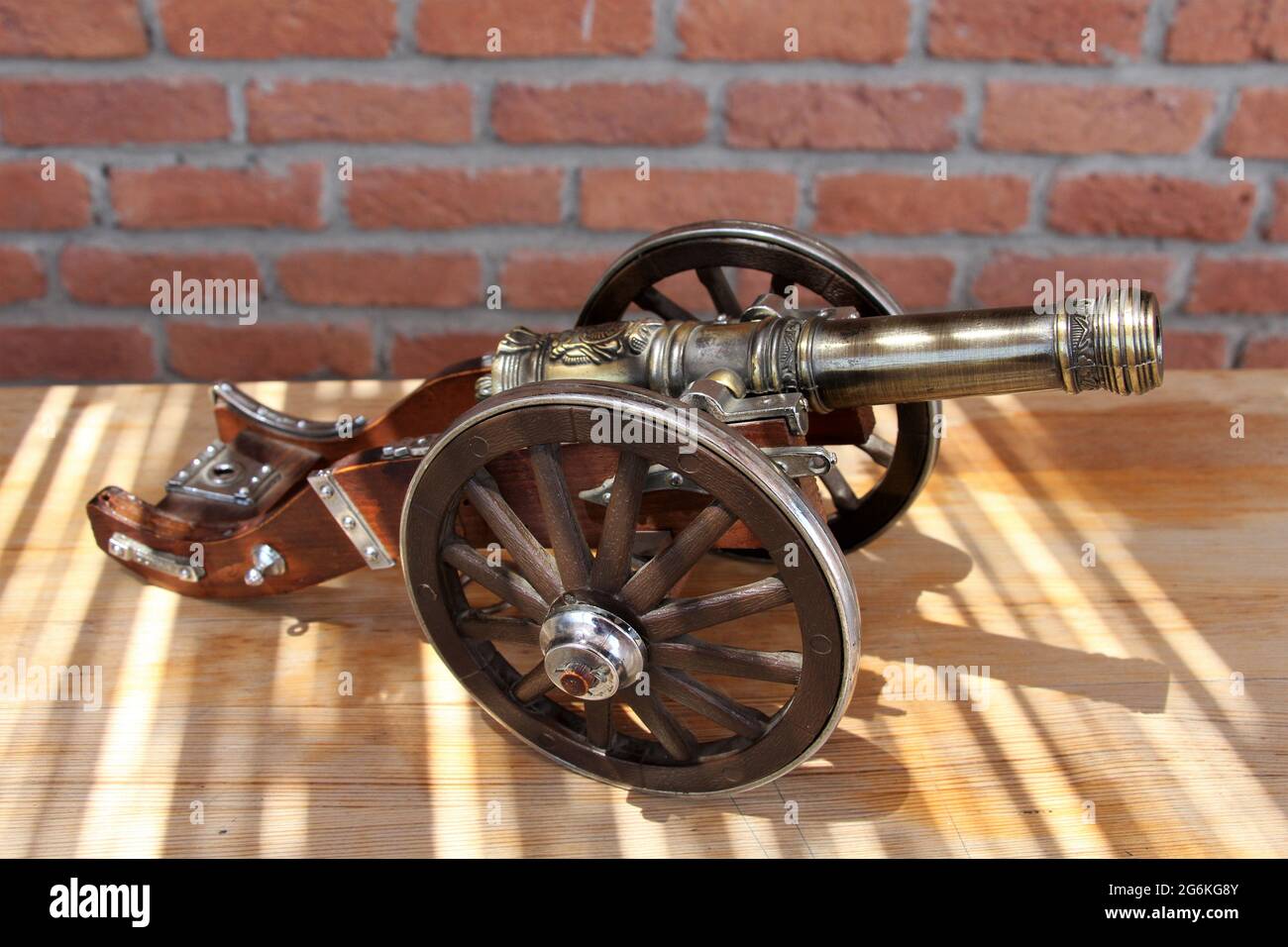 Ein Nachbau einer alten Kanonenpistole. Eine Kanonenpistole aus Bronze und Holz zur Dekoration. Im Hintergrund befindet sich eine Ziegelmauer. Stockfoto