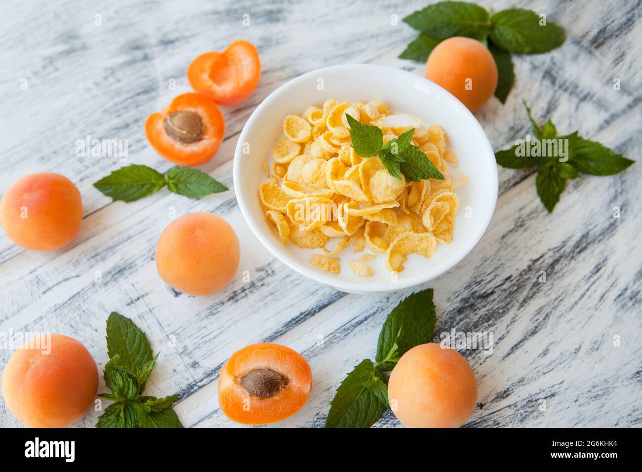 Maisflocken mit Aprikose am weißen Holztisch. Gesundes Sommerfrühstück, das aus verschiedenen gelben Zutaten besteht Stockfoto