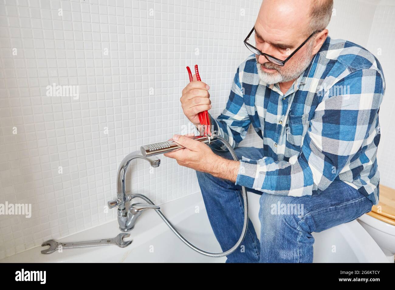 Ein Klempner als Handwerker repariert den Duschkopf und den Schlauch im Badezimmer Stockfoto