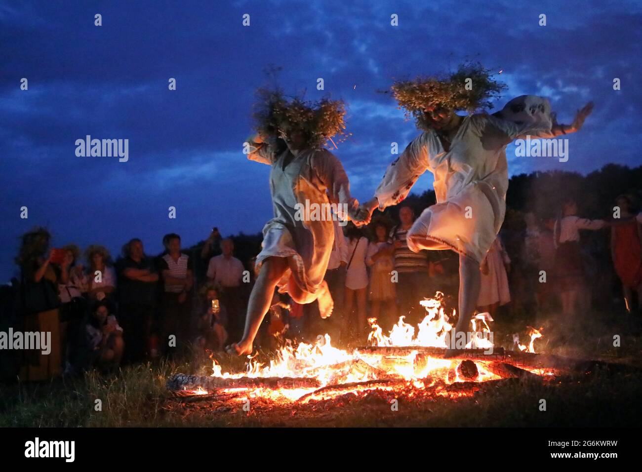 KIEW, UKRAINE - 6. JULI 2021 - Mädchen in Blumenkronen springen über das Lagerfeuer, während sie die Hände während der Kupala-Abendfeier im National halten Stockfoto