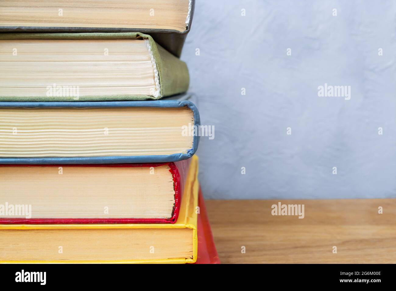 Stapel von bunten Hardback-Büchern auf Holztisch nah an grauen und blauen Betonwänden Stockfoto