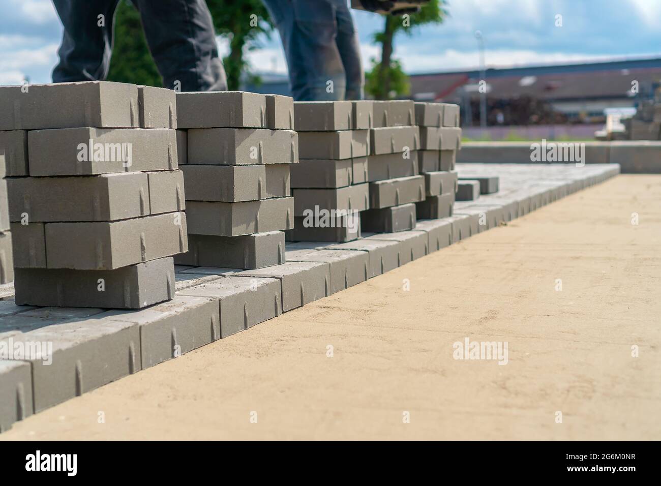 Die Füße des Menschen stehen in der Nähe einer großen Anzahl von Betonsteinen auf dem Boden. Konzept der Verlegung von Pflasterplatten Stockfoto