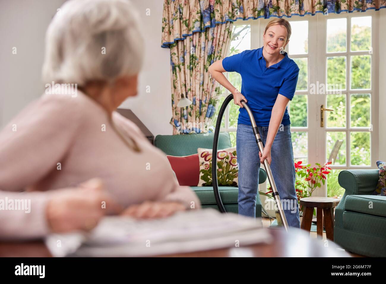 Weibliche Home Hilfe Reinigung Haus Mit Staubsauger Und Im Gespräch Mit Senior Frau Stockfoto