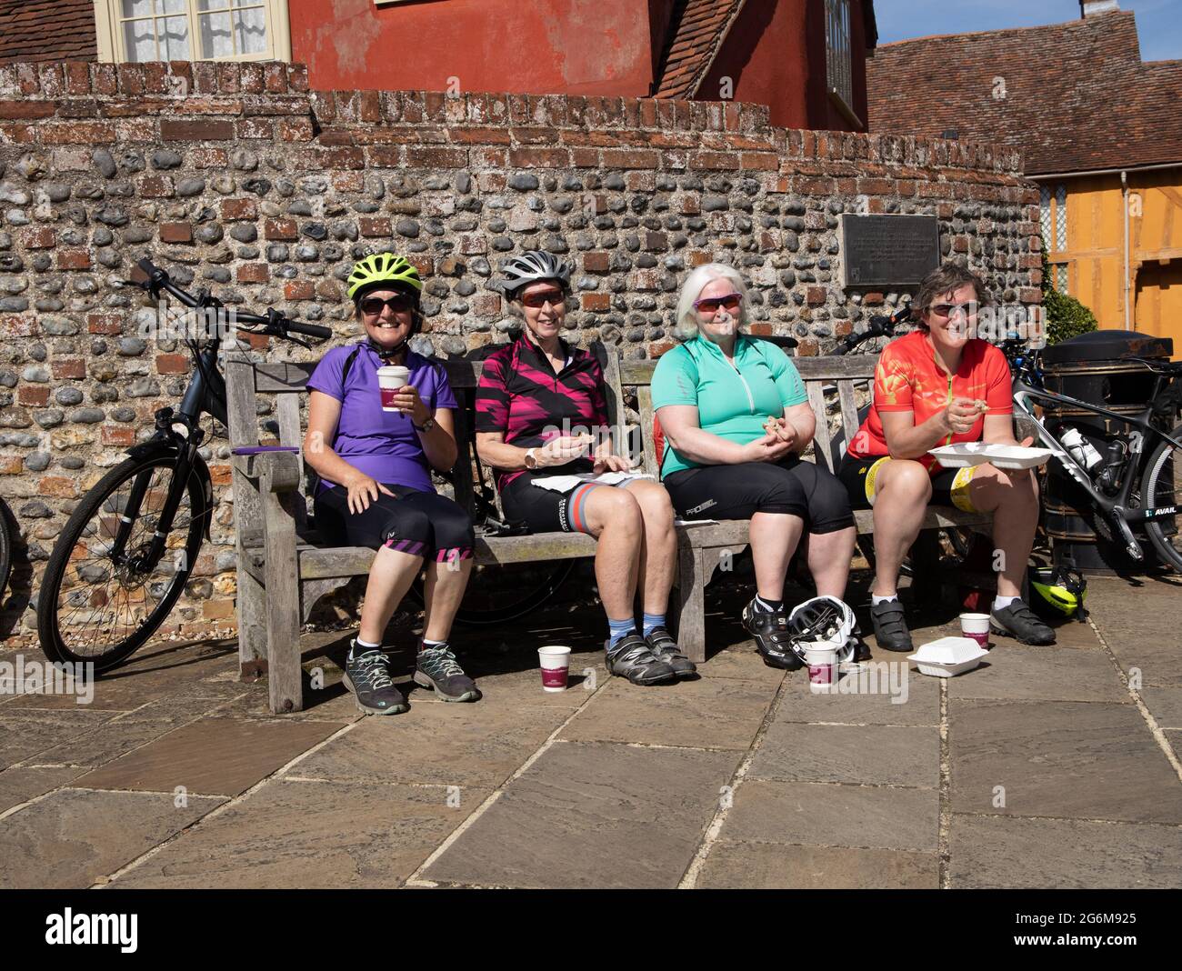 Vier glückliche ältere Radfahrerinnen essen und ruhen auf der Bank Lavenham Suffolk England Stockfoto