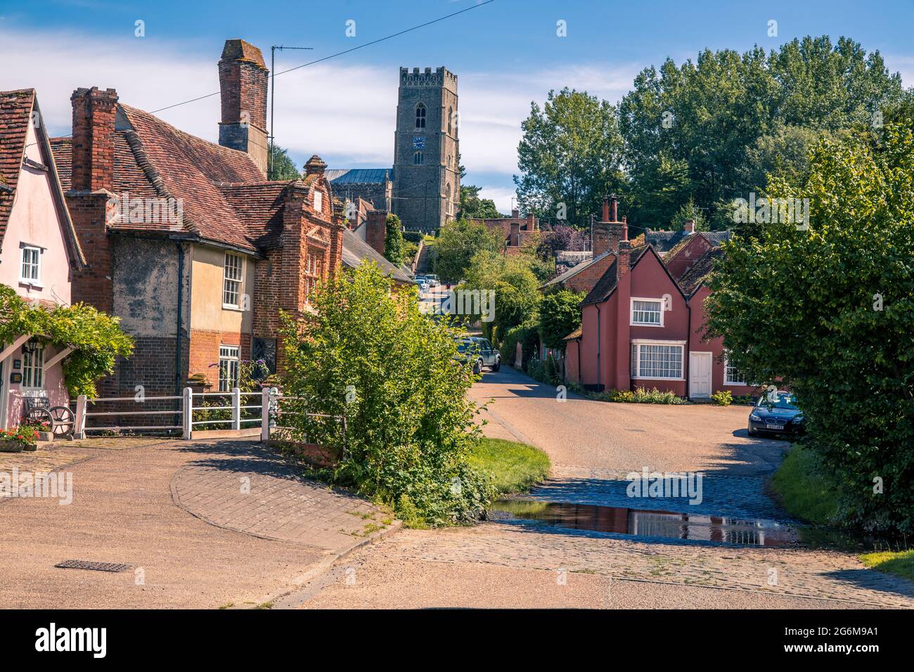 Gepflasterte furt über einen Bach und eine Reihe von Fachwerkhäusern an der Street Kersey Suffolk England und der Pfarrkirche oben Stockfoto