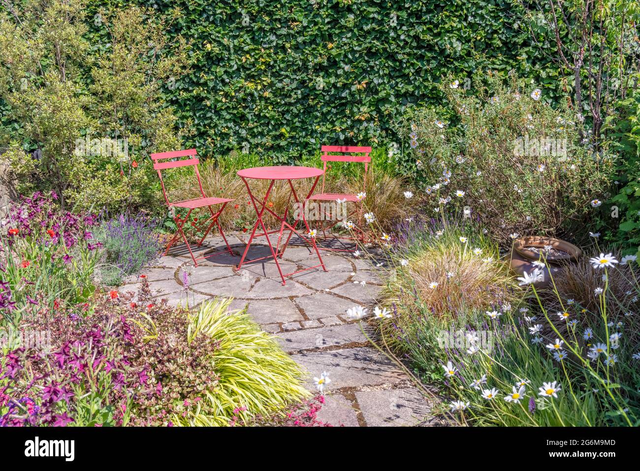 Ruhige, gekennzeichnete Gartenecke mit einem kleinen, rot gestrichenen Metallgartentisch und Stühlen. Stockfoto