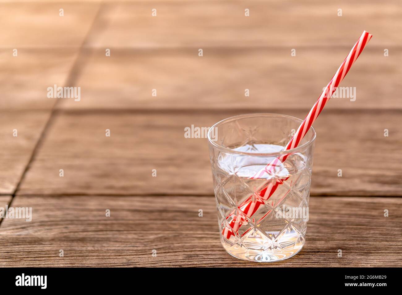 Glas Sodawasser mit rot-weiß gestreiftem Stroh auf Holztisch. Erfrischendes alkoholfreies Getränk für heiße Sommertage, um für eine Detox-Diät hydratisiert zu bleiben. Stockfoto