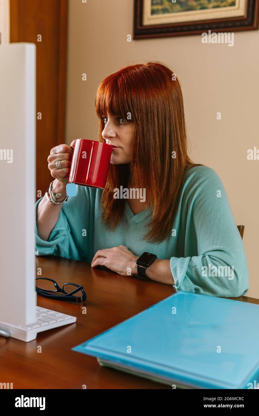 Vertikales Foto einer Frau, die vor dem Computer Tee trinkt Stockfoto