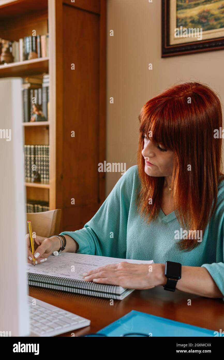 Vertikales Foto einer Frau, die während der Telearbeit in einem Notebook schreibt Stockfoto