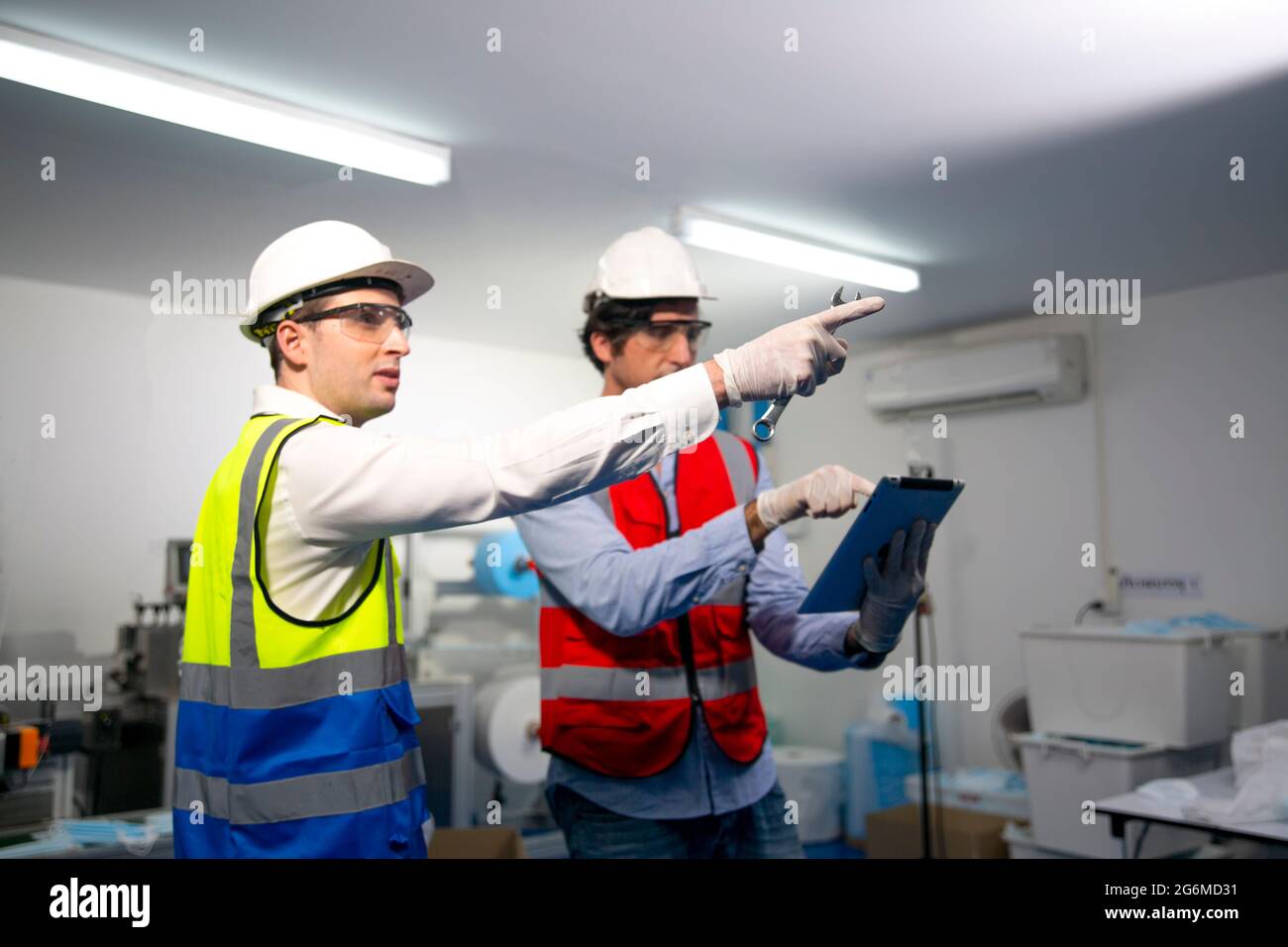 Männliche Ingenieure mit mittlerem Erwachsenenalter untersuchen Maschinenteile an einer Produktionslinie medizinischer Masken in einer Fabrik. Stockfoto