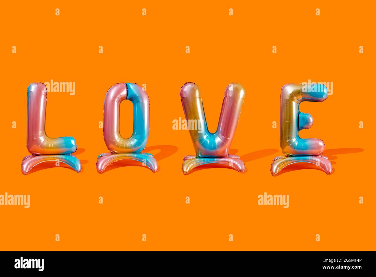 Vier bunte, buchstabenförmige Luftballons bilden das Wort Liebe auf einem orangefarbenen Hintergrund Stockfoto