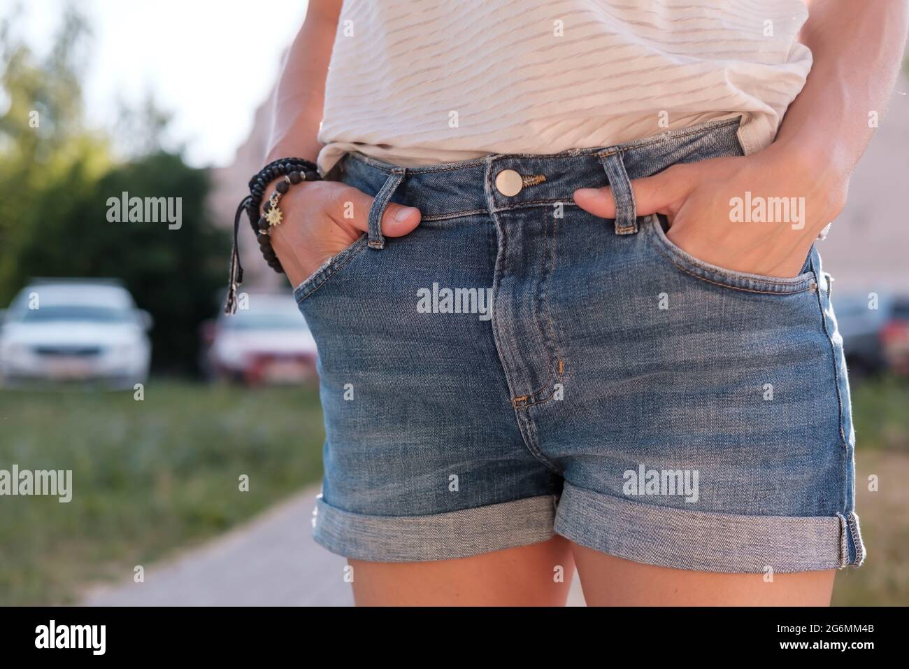 Frau steckte ihre Hände in die Taschen von Denim-Shorts, während sie an einem Sommertag im Freien stand. Nahaufnahme. Stockfoto