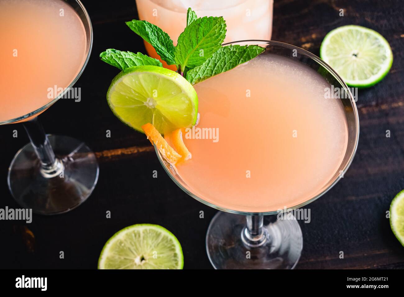 Rosa Grapefruit-Martinis mit Garnierung: Zitrusmartinis garniert mit Minzzweigen, Limettenscheiben und rosa Grapefruitdrehungen Stockfoto