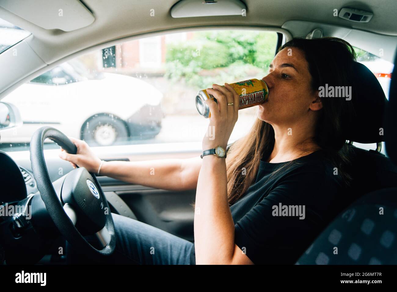 Eine Frau in den dreißiger Jahren trinkt aus einer Dose Bier, während sie mit dem Auto fährt Stockfoto