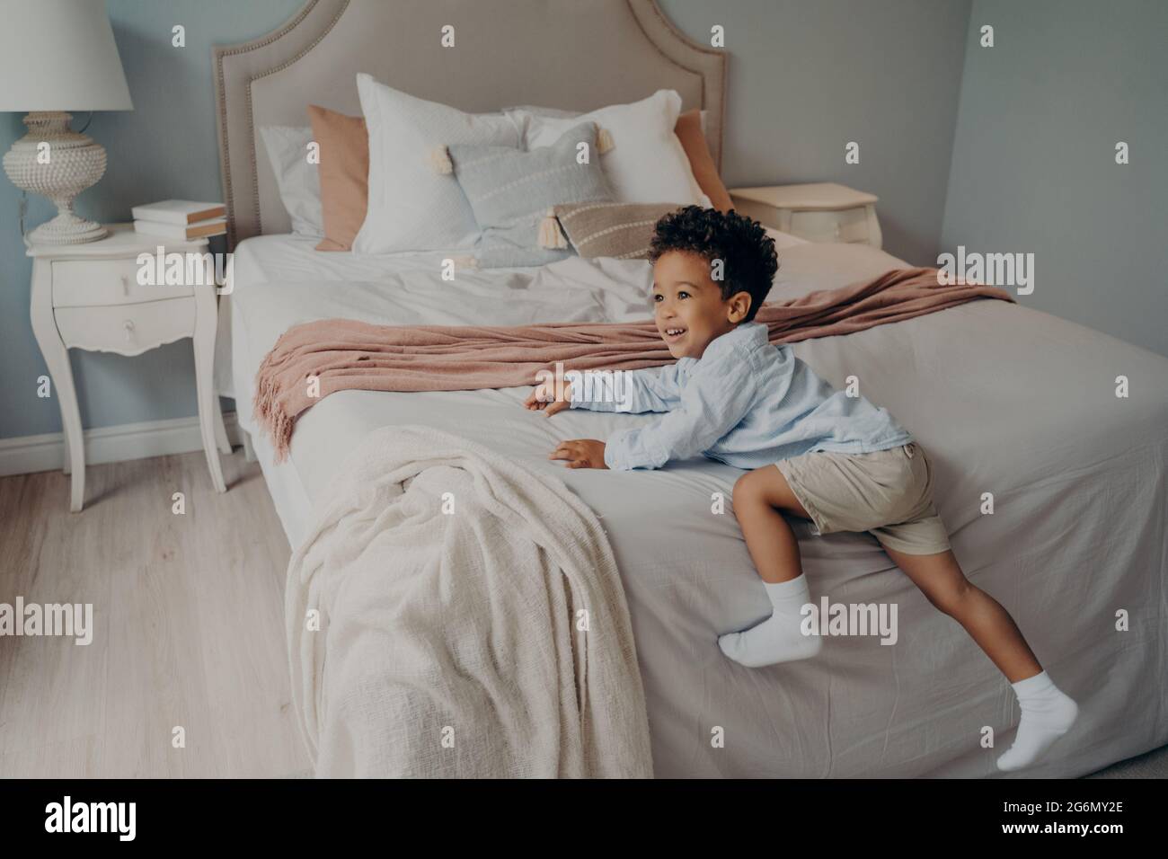 Fröhliches kleines afroamerikanisches Kind, das drinnen auf dem Bett spielerisch ist Stockfoto