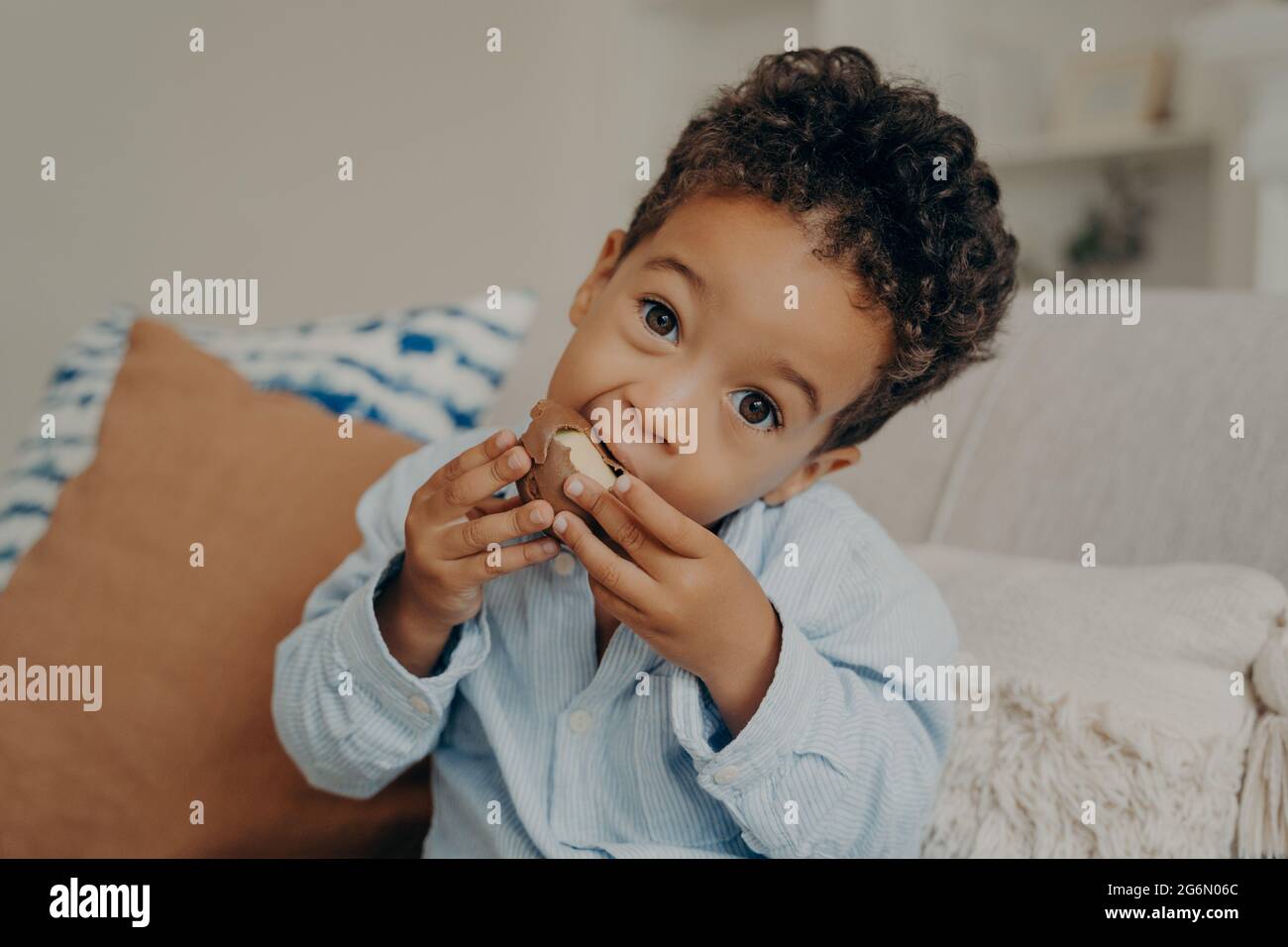 Niedlicher Mulatto-Junge mit großen Haselaugen, der zu Hause Süßigkeiten isst Stockfoto