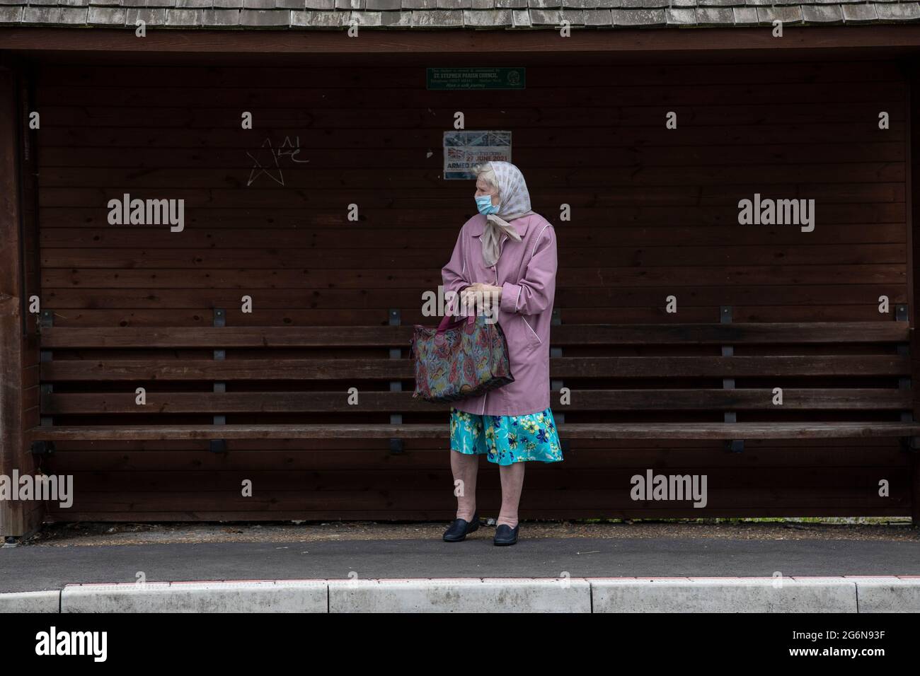 Eine ältere Dame stand an einer Bushaltestelle und wartete darauf, dass der nächste Bus an einem stürmischen Tag eintreffen sollte, England, Vereinigtes Königreich, Vereinigtes Königreich Stockfoto