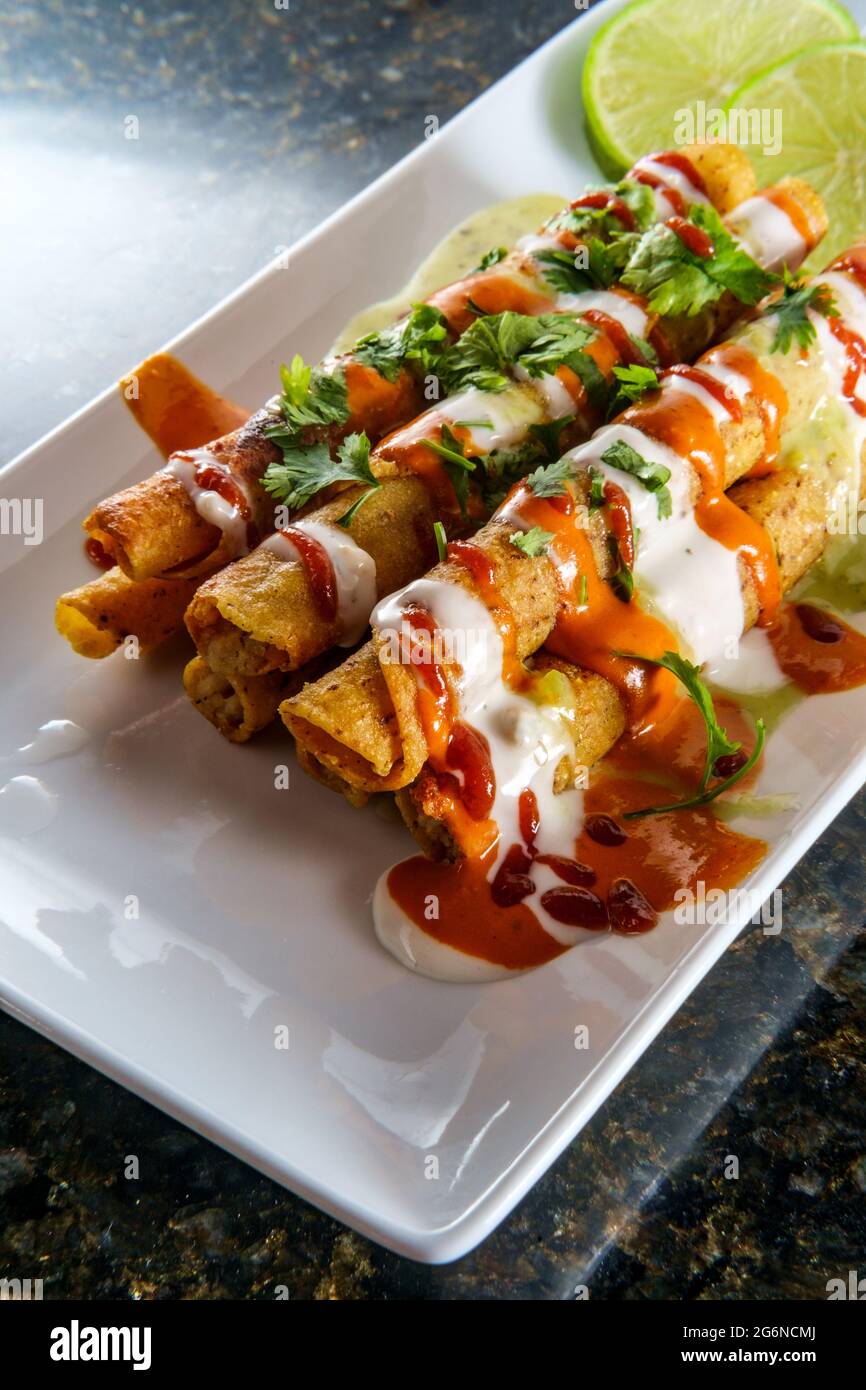 Mexikanisches Huhn und Käse gerollt Taco Taquitos in heißen Saucen und Creme fraiche erstickt Stockfoto