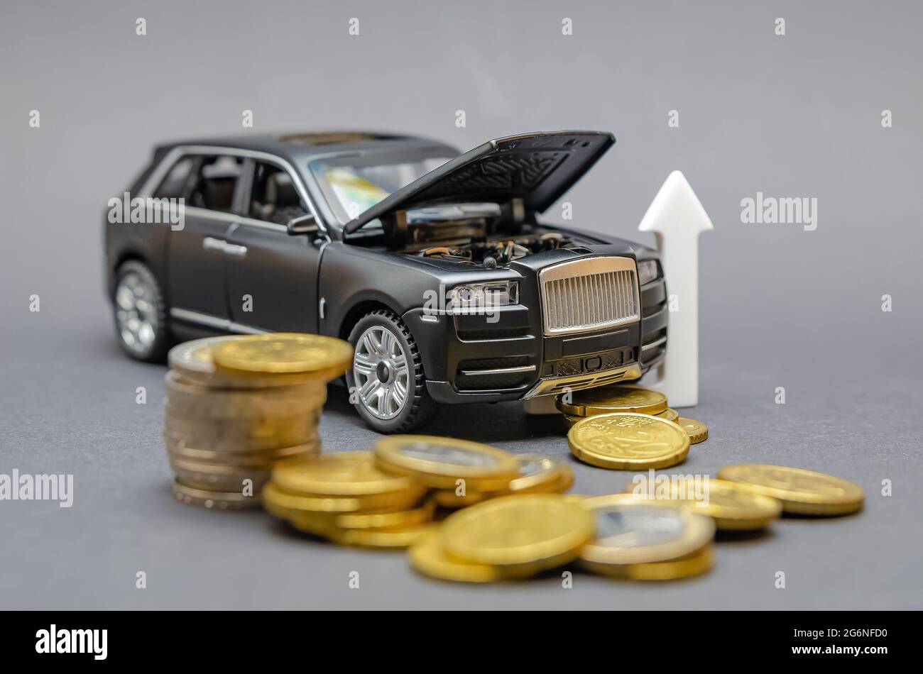 Steigende Preise für Autoteile. Auf einem schwarzen Hintergrund befindet sich ein Modellauto mit einer erhöhten Haube, um eine Münze herum. Car Service Preissteigerung Konzept. Stockfoto