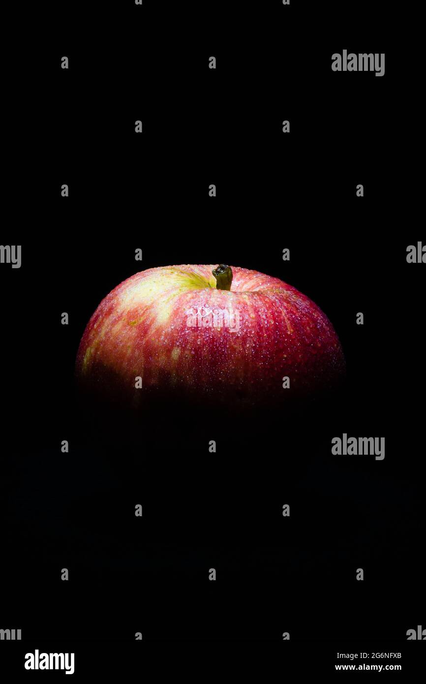 Dunkles, tiefes Bild eines frischen und reifen roten Apfels, der nur von oben beleuchtet wird Stockfoto