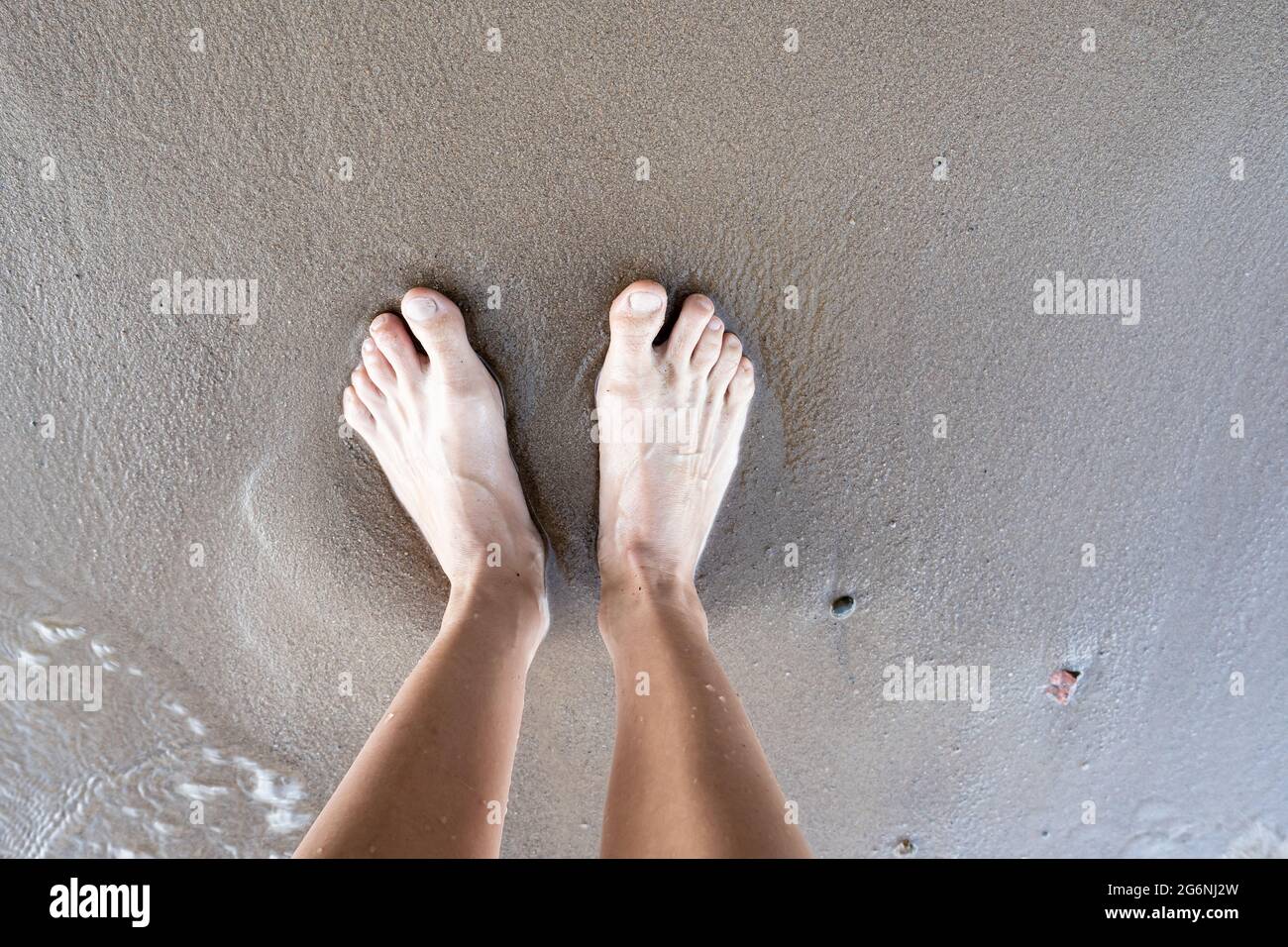An einem Sommertag stehen nasse weibliche gebräunte Beine auf einem sandigen Flussufer. Lifestyle. Draufsicht. Stockfoto