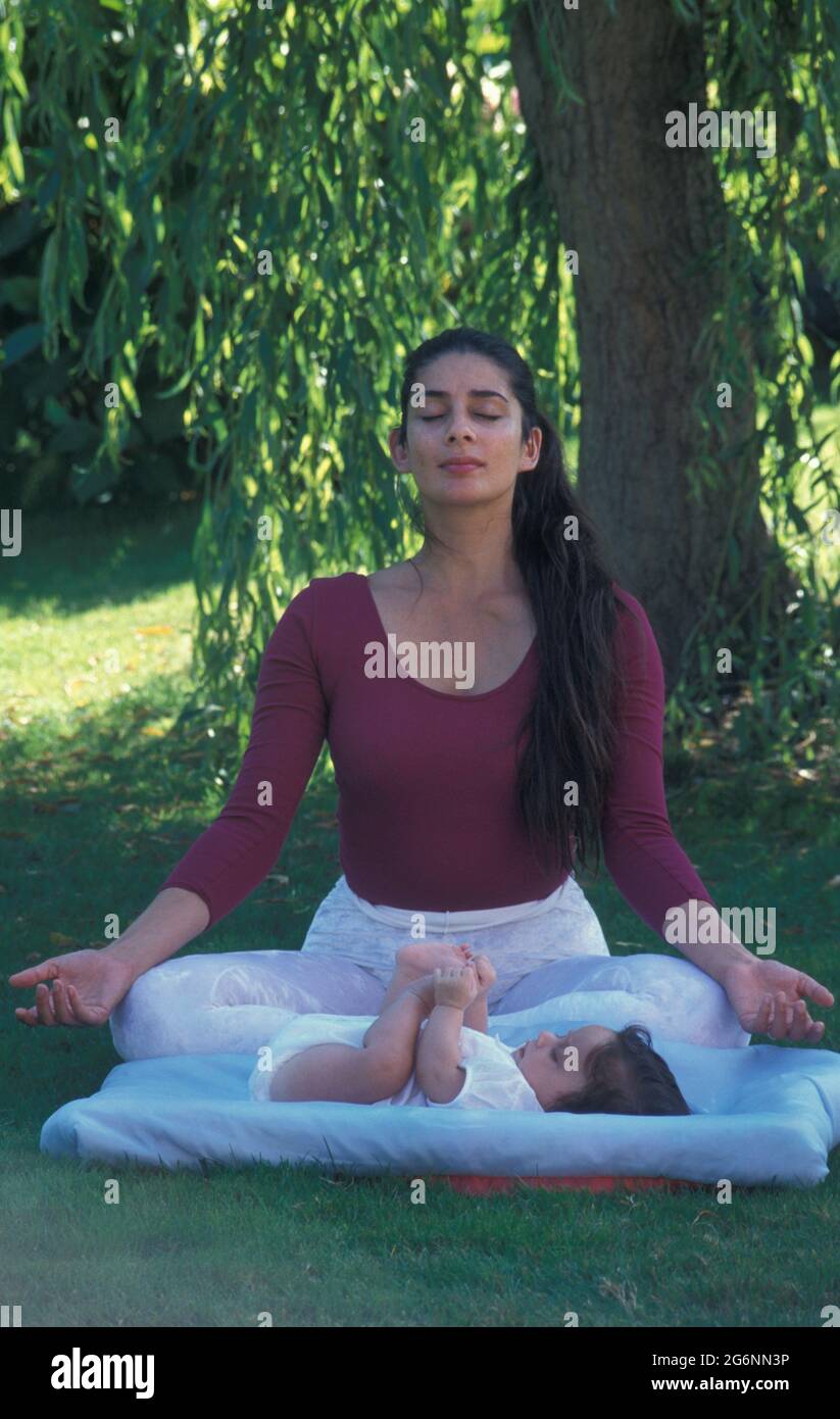 Frau, die draußen mit ihrem neugeborenen Baby Yoga macht Stockfoto