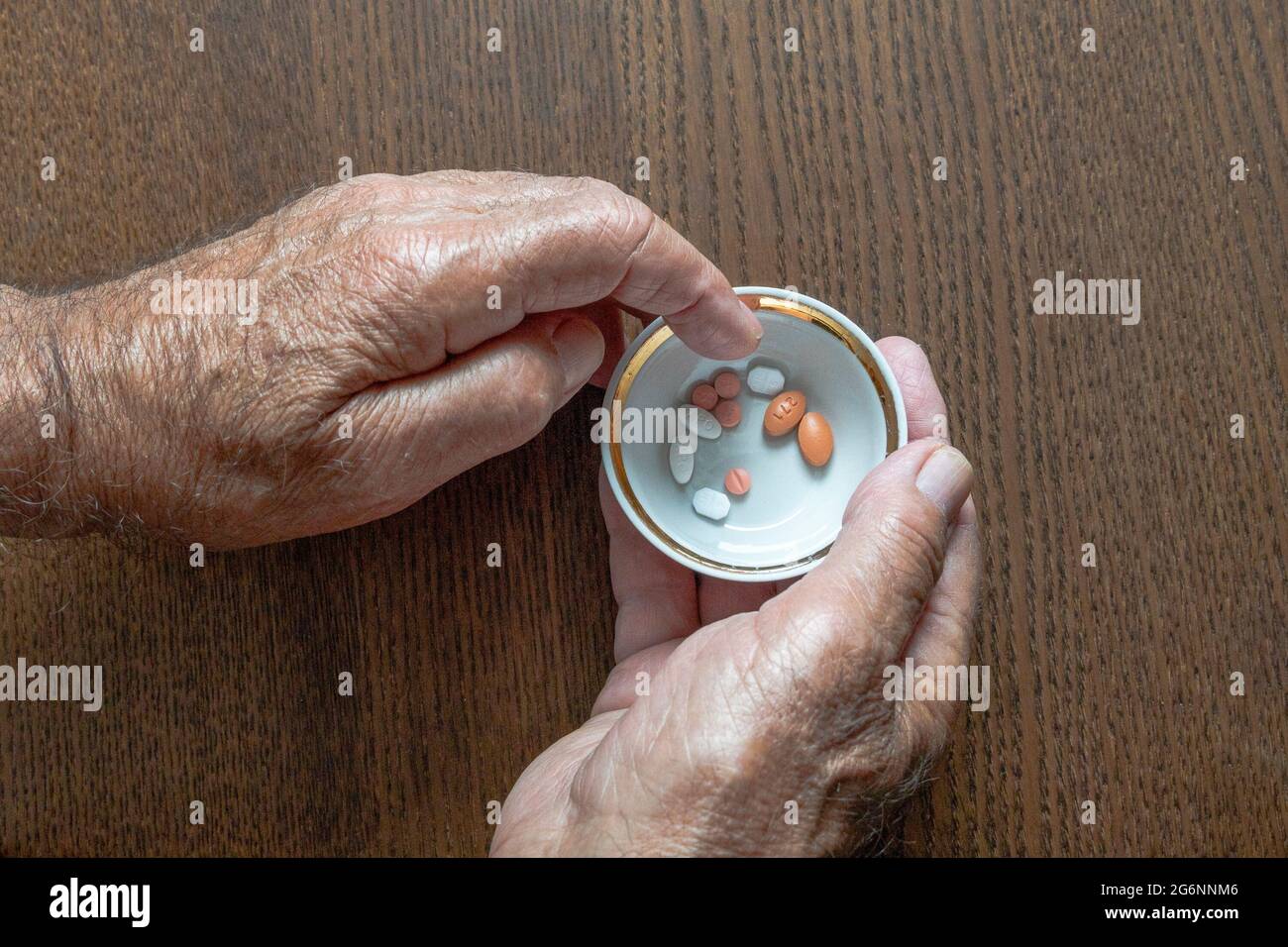 Ein älterer Mann, der eine Tasse Pillen in den Händen hält, wählt daraus die gewünschte Pille aus Stockfoto