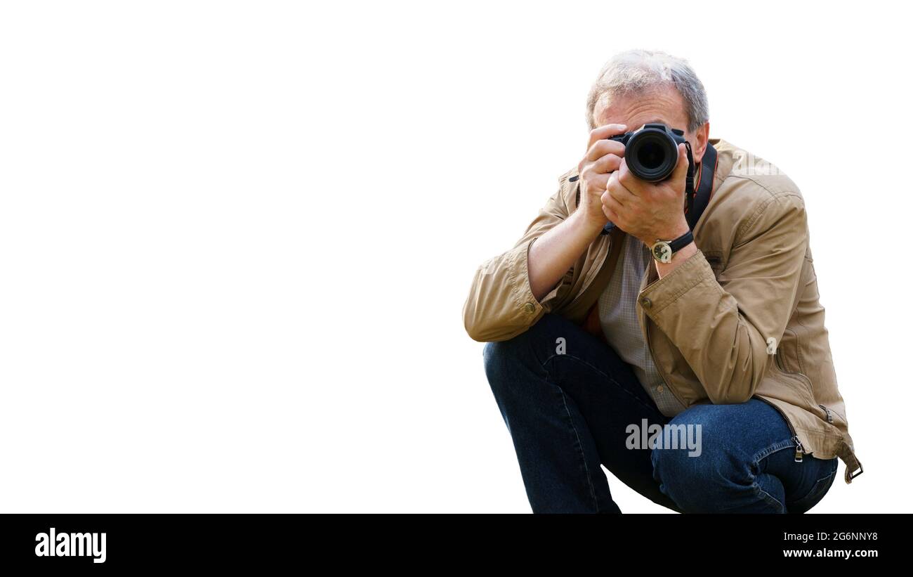 Ein Mann mittleren Alters mit einer Kamera macht beim Hocken Fotos. Im Vordergrund richtet sich die Kamera an den Betrachter. Ein erfahrener Fotograf, iso Stockfoto