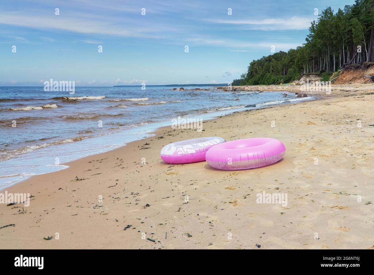 Zwei rosa Schwimmringe / Schwimmschläuche / Innenschläuche am Sandstrand mit blauem Himmel und Meer im Hintergrund. Speicherplatz kopieren. Stockfoto