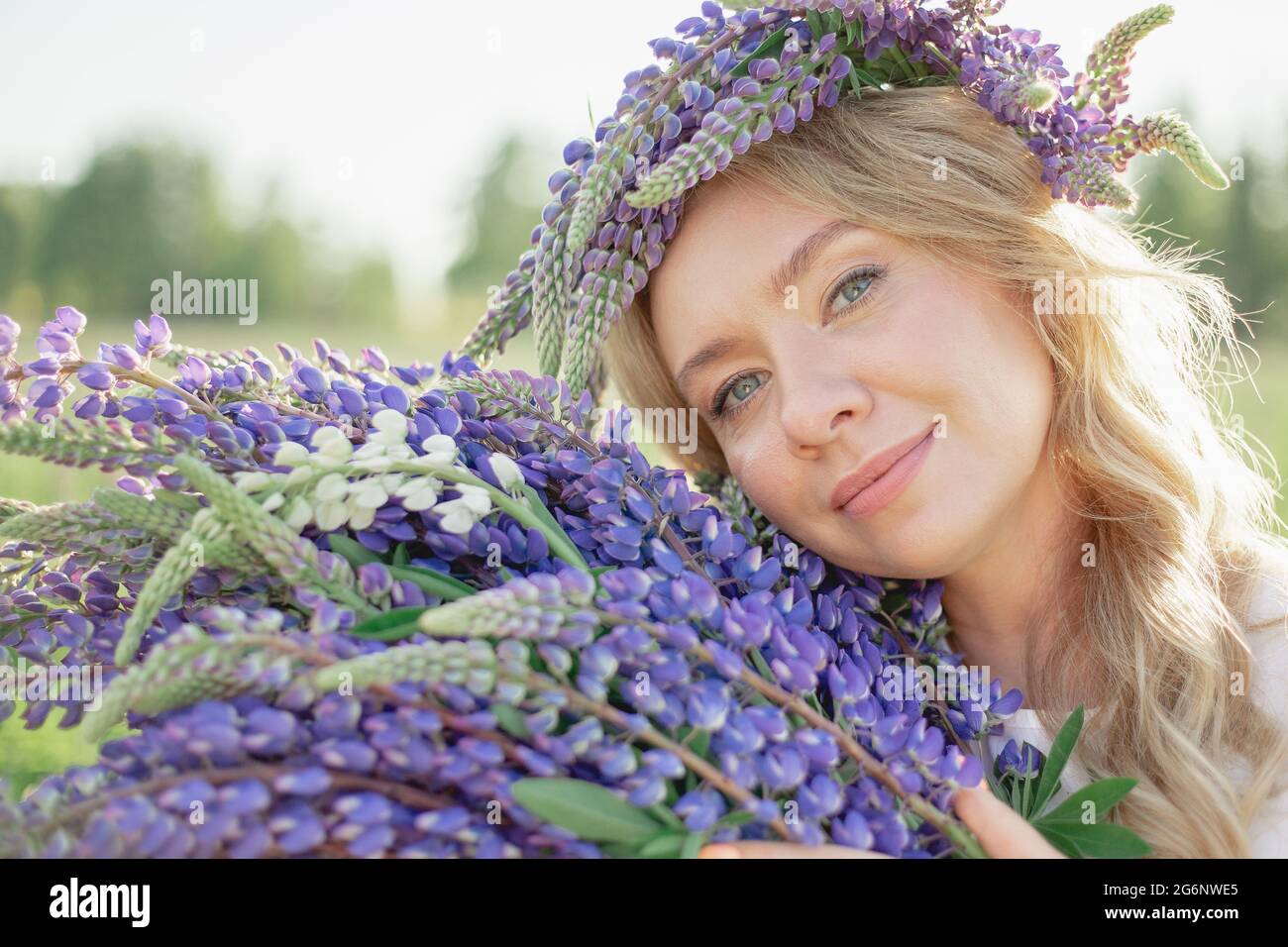 Ein hippes Mädchen, das einen Blumenstrauß in den Händen hält. Mädchen versteckte ihr Gesicht hinter einem Blumenstrauß aus Lupinen. Mädchen hält große Bouquet von lila Lupinen in einem Stockfoto