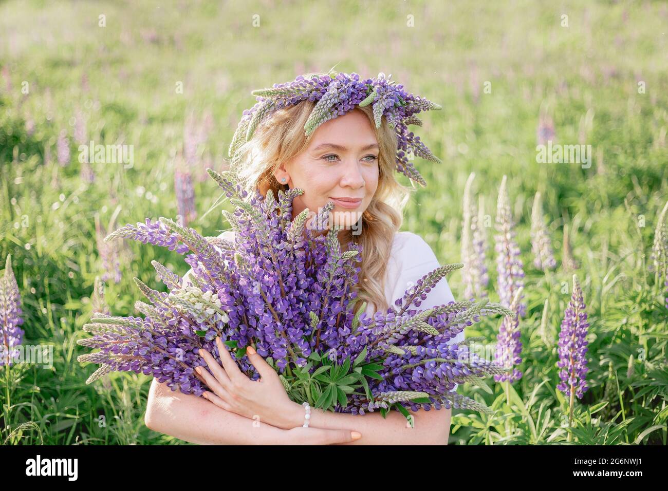 Ein hippes Mädchen, das einen Blumenstrauß in den Händen hält. Mädchen versteckte ihr Gesicht hinter einem Blumenstrauß aus Lupinen. Mädchen hält große Bouquet von lila Lupinen in einem Stockfoto