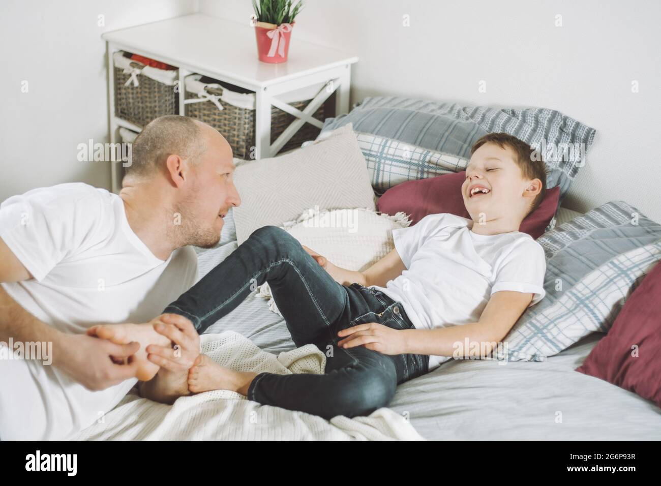 Vater spielt mit seinem Sohn 7-10 auf dem Bett. Papa kitzelt die Füße der Kinder. Familie, die Spaß hat Stockfoto