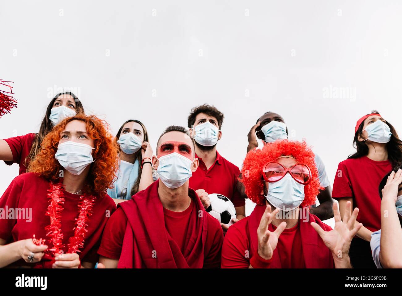 Multirassische Menschen tragen eine schützende Gesichtsmaske und beobachten Fußballspiele Stockfoto