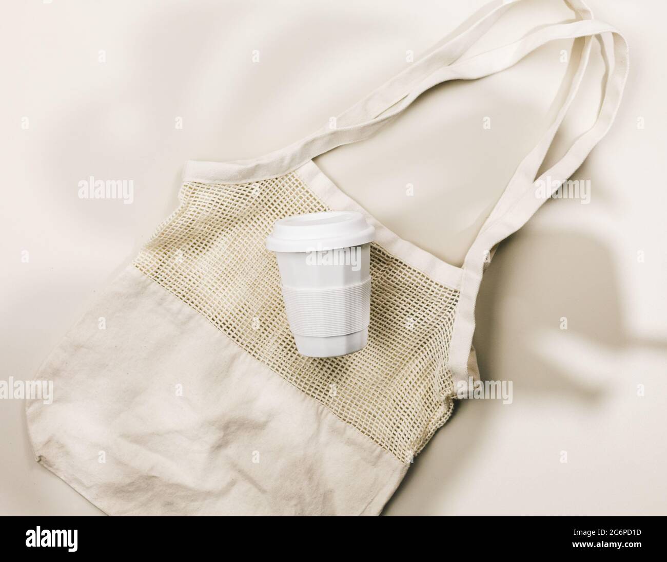 Wiederverwendbarer Beutel aus beigefarbenem Baumwollgewebe und Kaffeebecher auf beigefarbenem Hintergrund. Umweltfreundliche Einkaufstasche. Nahaufnahme. Zero Waste Lebensmittelkonzept. Nachhaltiges Leben Stockfoto