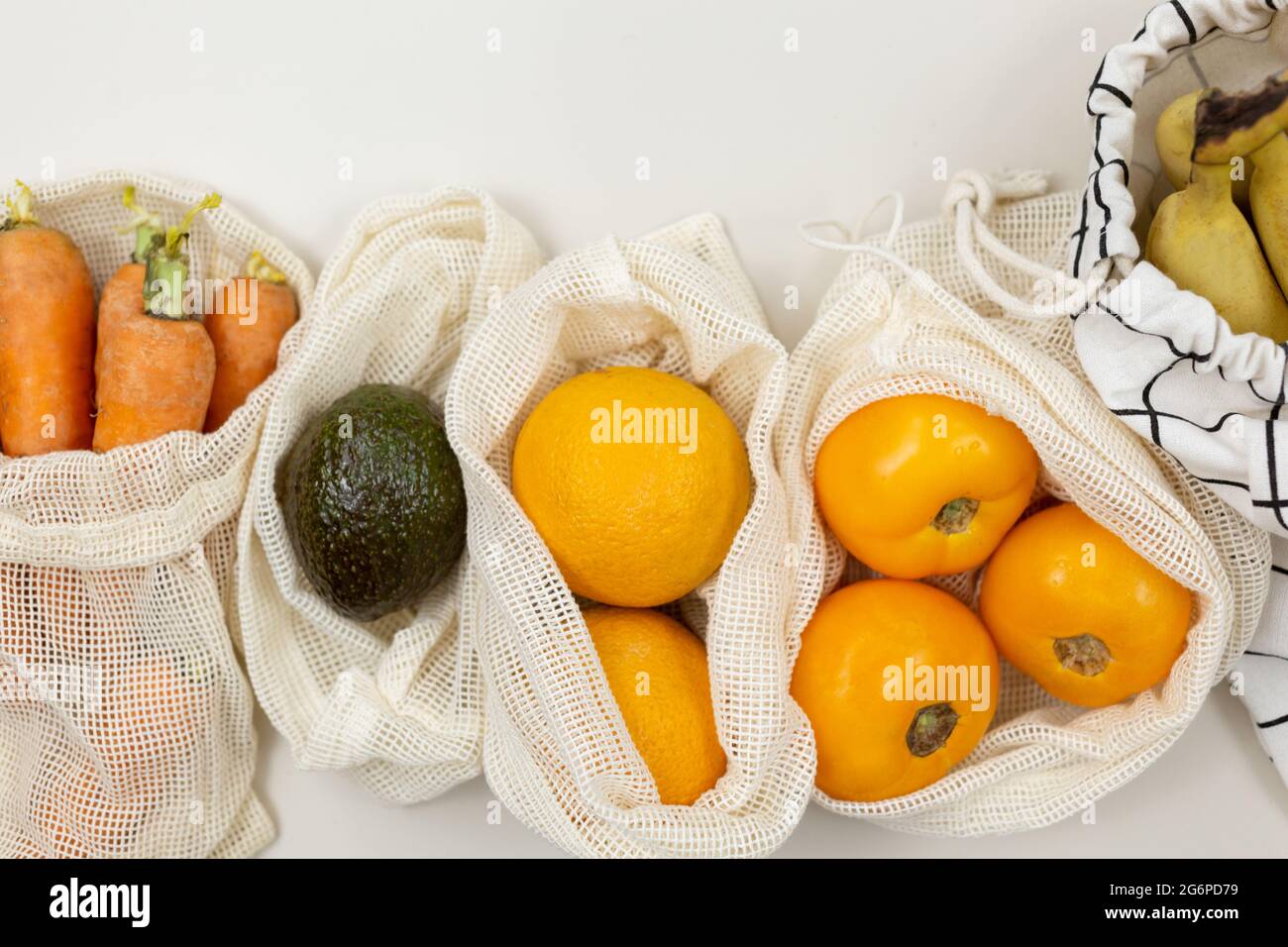 Frisches Obst, Gemüse in Öko-Baumwollbeuteln auf einem beigen Tisch. Karotten, Orangen, Bananen, Avocado vom Markt. Zero Waste Shopping-Konzept. Stockfoto