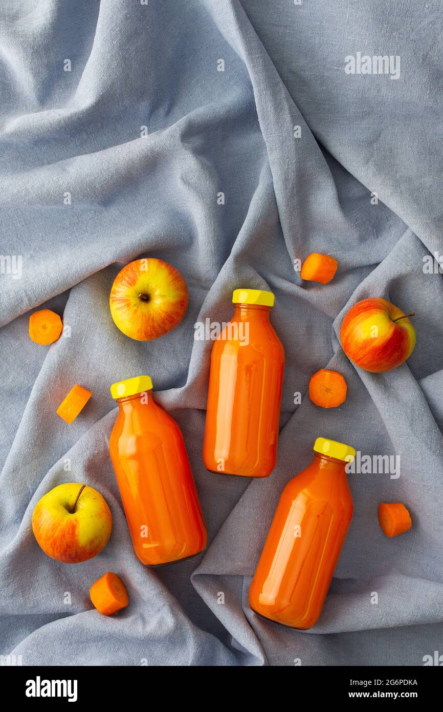 Karotten-Apfelsaft in Flaschen mit frischen Äpfeln und Karotten auf blauer Tischdecke, Draufsicht Stockfoto