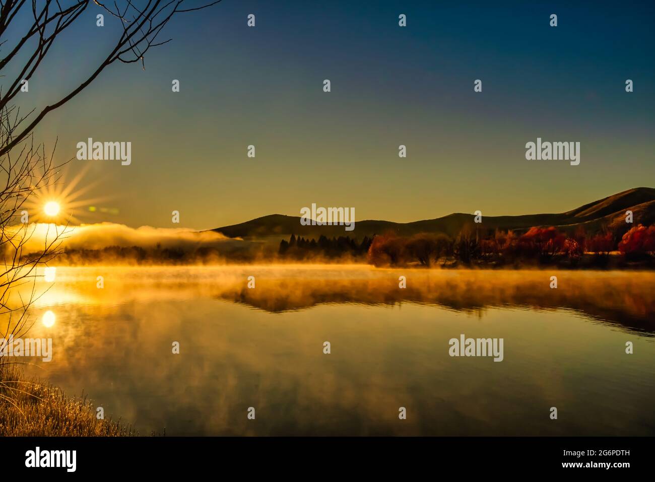 Sonneneinstrahlung und Bergreflexionen schweben über der Wasseroberfläche am verlassenen See bei Sonnenaufgang im Nebel und in der niedrigen Wolke Stockfoto