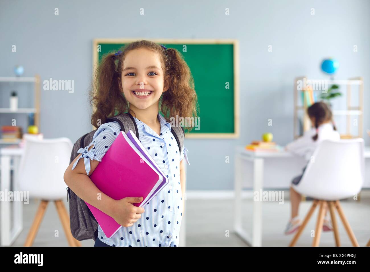 Zurück zur Schule. Lächelndes Schulmädchen mit einem Buch in der Hand schaut in der Klasse auf die Kamera. Stockfoto