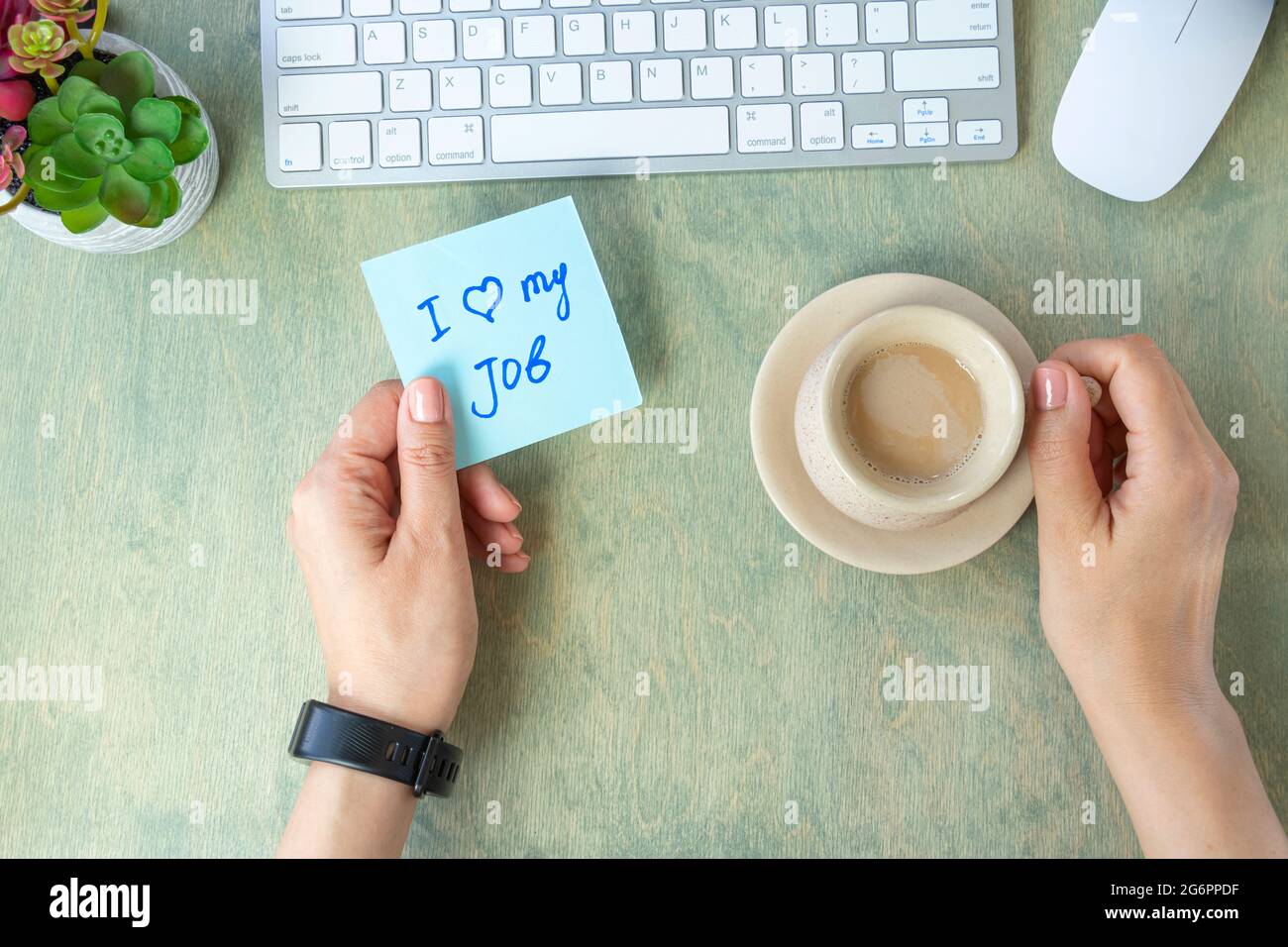 Weibliche Hände halten Notiz mit Worten, ich liebe meinen Job, Tasse Kaffee, Tastatur, Kaktus und Mause auf einem Holztisch. Konzept für gute Arbeit. Draufsicht auf dem Desktop. Flach liegend Stockfoto