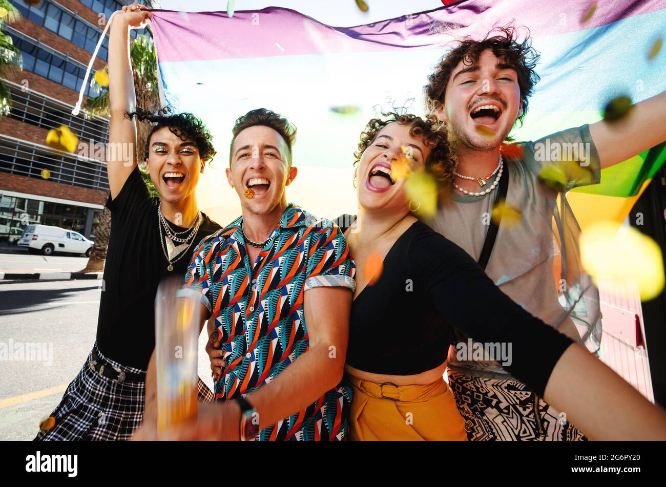 Gruppe von nicht-konformen jungen Menschen, die mit der Flagge des Regenbogens feiern. Vier queere Menschen lächeln fröhlich während der Feier Stockfoto