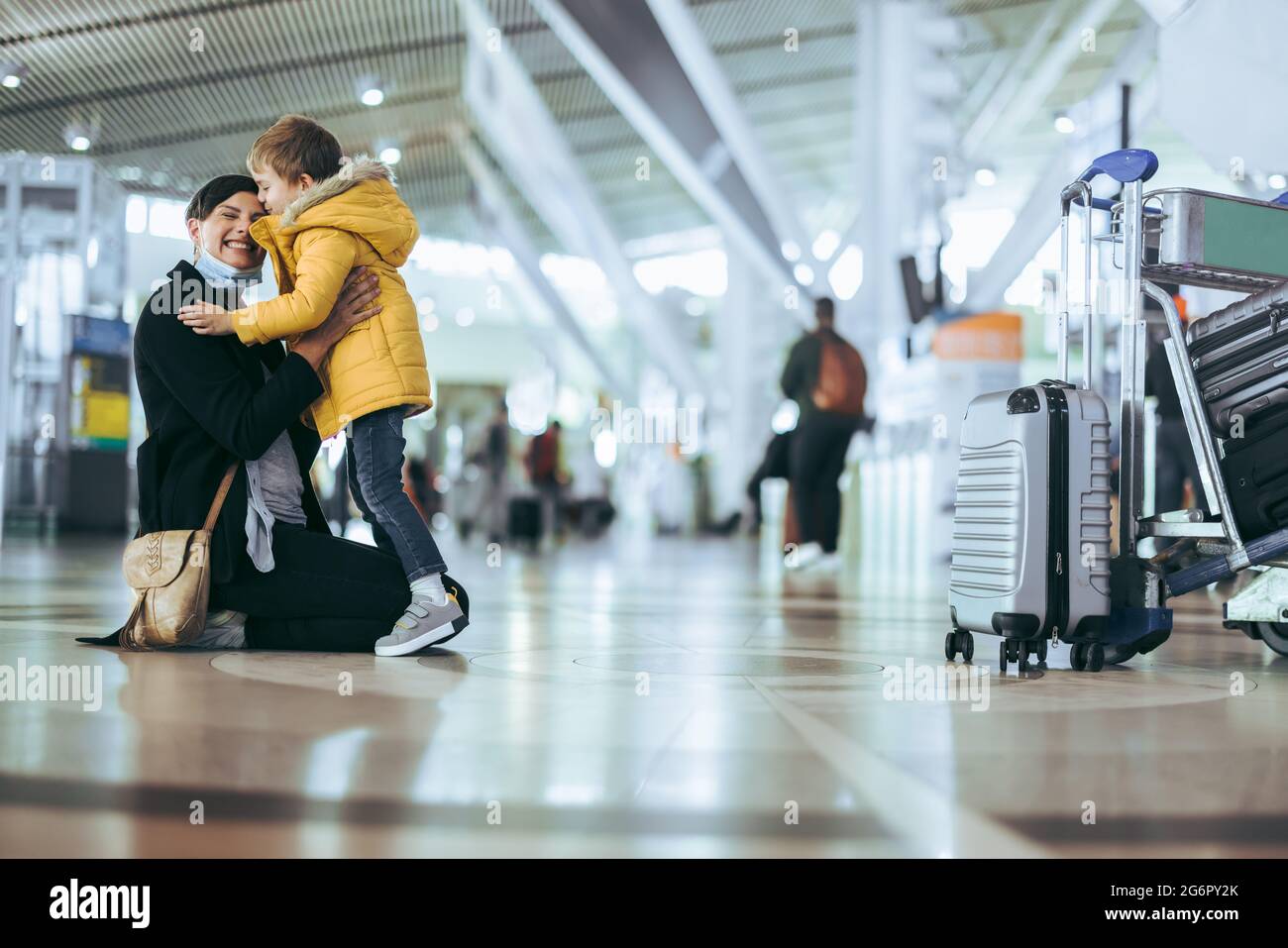 Mutter und Kind treffen sich nach einer Pandemie am Flughafen. Frau in Gesichtsmaske trifft Sohn nach der Ankunft von der Reise am Flughafen. Stockfoto