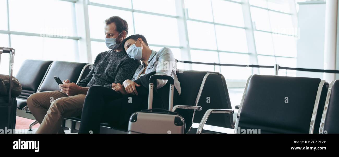 Mann und Frau mit Gesichtsmasken sitzen in der Wartelounge des Flughafenterminals. Reisenpaar strandete während Corona-Virus-Ausbruch am Flughafen. Stockfoto