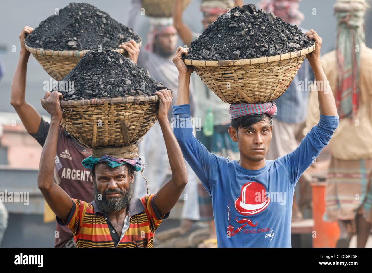 Eine menschliche Kette von Trägern trägt Kohle, Sand und Kies von den Bargen, die an der Aminbazar Landing Station am Buriganga River außerhalb von Dhaka festgemacht sind. Bangladesch absolviert derzeit den Abschluss der LDC-Kategorie (am wenigsten entwickelte Länder), was zum großen Teil der extrem harten Arbeit billiger Arbeitskräfte zu verdanken ist. Ein Portier macht zwischen 80 und 140 USD pro Monat, laut den Websites paylab.com und averagesalarysurvey.com Stockfoto