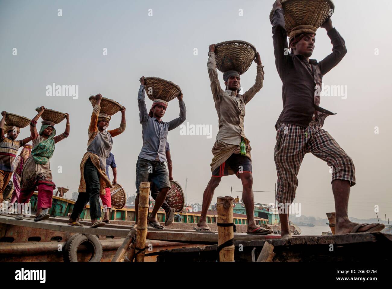Eine menschliche Kette von Trägern trägt Kohle, Sand und Kies von den Bargen, die an der Aminbazar Landing Station am Buriganga River außerhalb von Dhaka festgemacht sind. Bangladesch absolviert derzeit den Abschluss der LDC-Kategorie (am wenigsten entwickelte Länder), was zum großen Teil der extrem harten Arbeit billiger Arbeitskräfte zu verdanken ist. Ein Portier macht zwischen 80 und 140 USD pro Monat, laut den Websites paylab.com und averagesalarysurvey.com Stockfoto