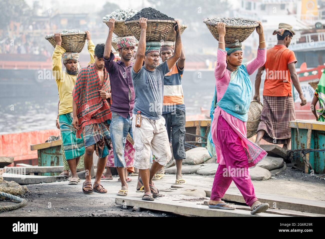 Eine menschliche Kette von Trägern trägt Kohle, Sand und Kies von den Bargen, die an der Aminbazar Landing Station am Buriganga River außerhalb von Dhaka festgemacht sind. Bangladesch absolviert derzeit den Abschluss der LDC-Kategorie (am wenigsten entwickelte Länder), was zum großen Teil der extrem harten Arbeit billiger Arbeitskräfte zu verdanken ist. Ein Portier macht zwischen 80 und 140 USD pro Monat, laut den Websites paylab.com und averagesalarysurvey.com Stockfoto